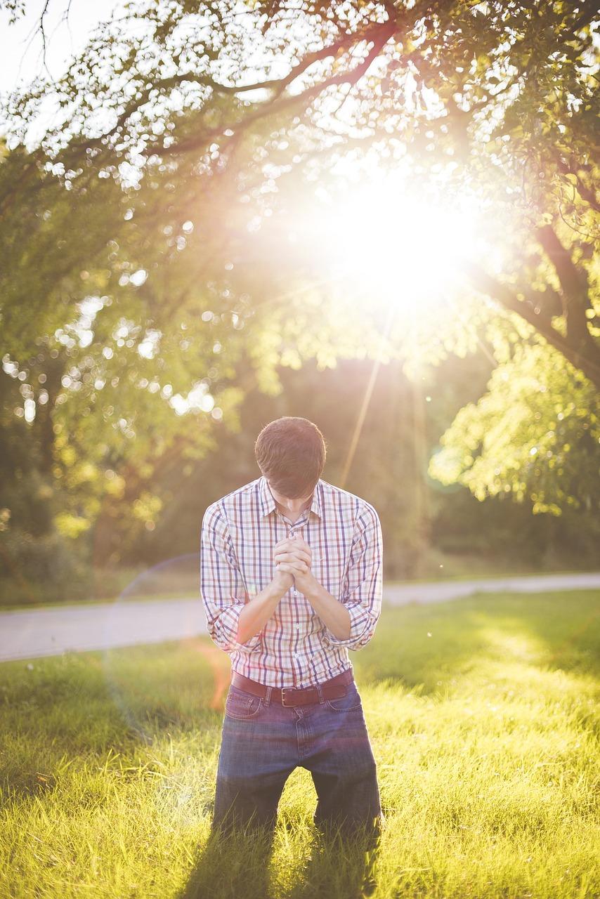 Hombre orando de rodillas en el pasto. Practicando cómo hacer una oración a Dios correctamente